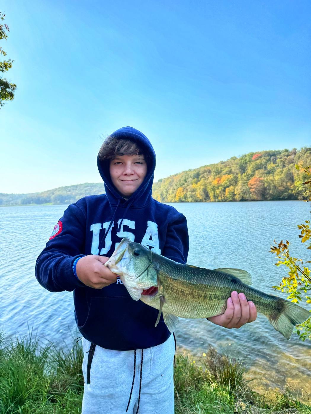 A boy holding a largemouth bass at the lakeshore