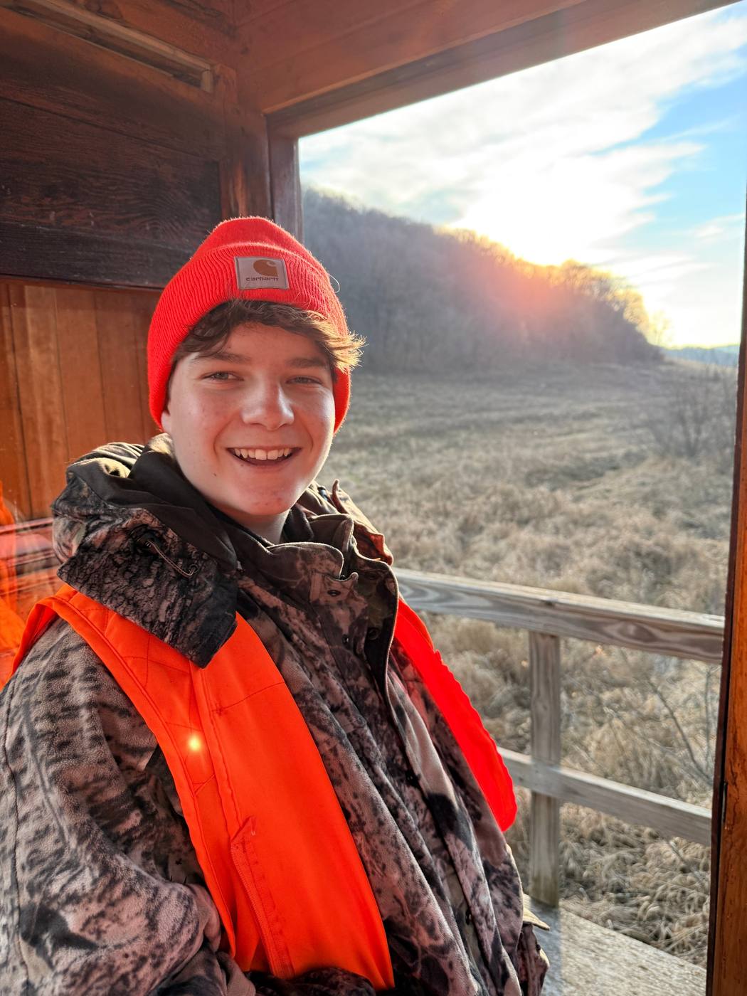 A teenager in blaze orange in a deer stand overlooking a frosty meadow