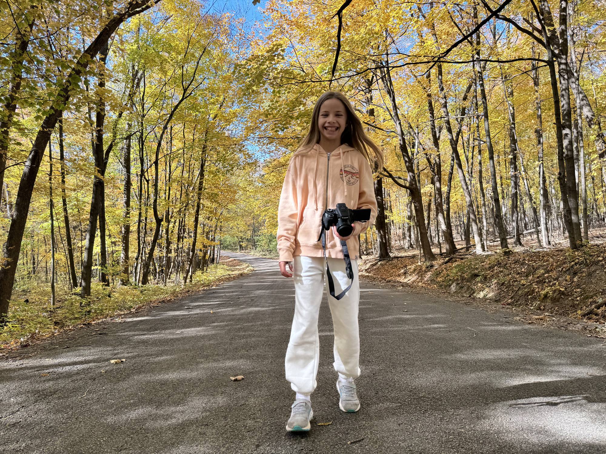A girl with a camera on a road through autumn woods