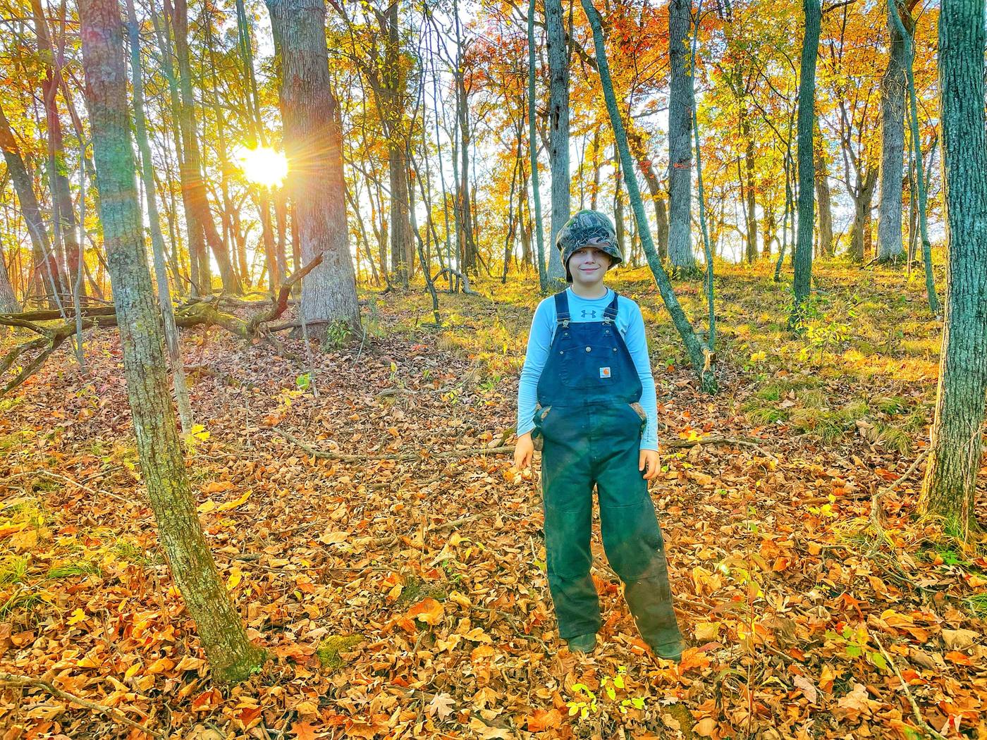 A boy in overalls among oaks in autumn light