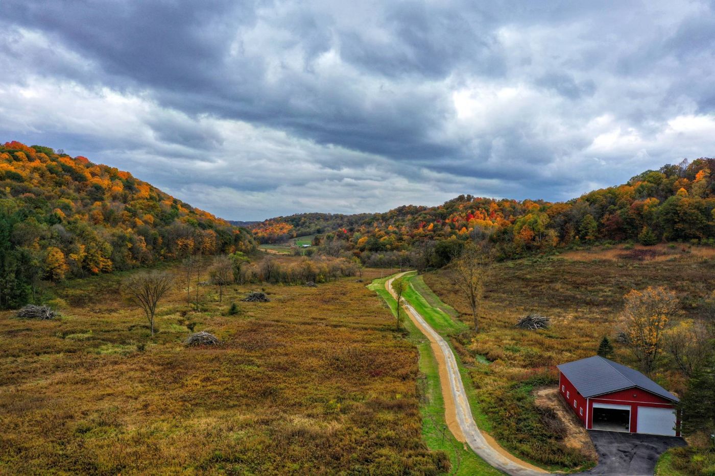 Bear Valley from above in fall: open meadow and prairie between wooded ridges in autumn color, with a gravel lane and a red barn